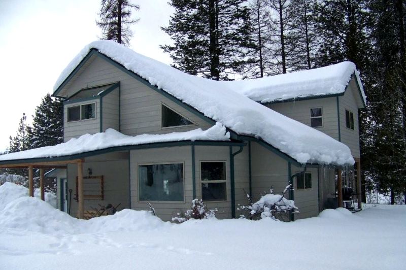 the same house under deep snow, with a foot of snow on both roof slopes and icicles at the eaves